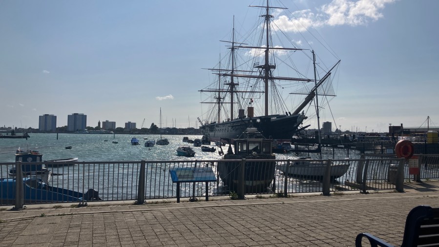HMS Warrior (1860), a historic iron hulled Royal Navy warship with tall masts and rigging, photographed across Portsmouth Harbour at Portsmouth Historic Dockyard, England.