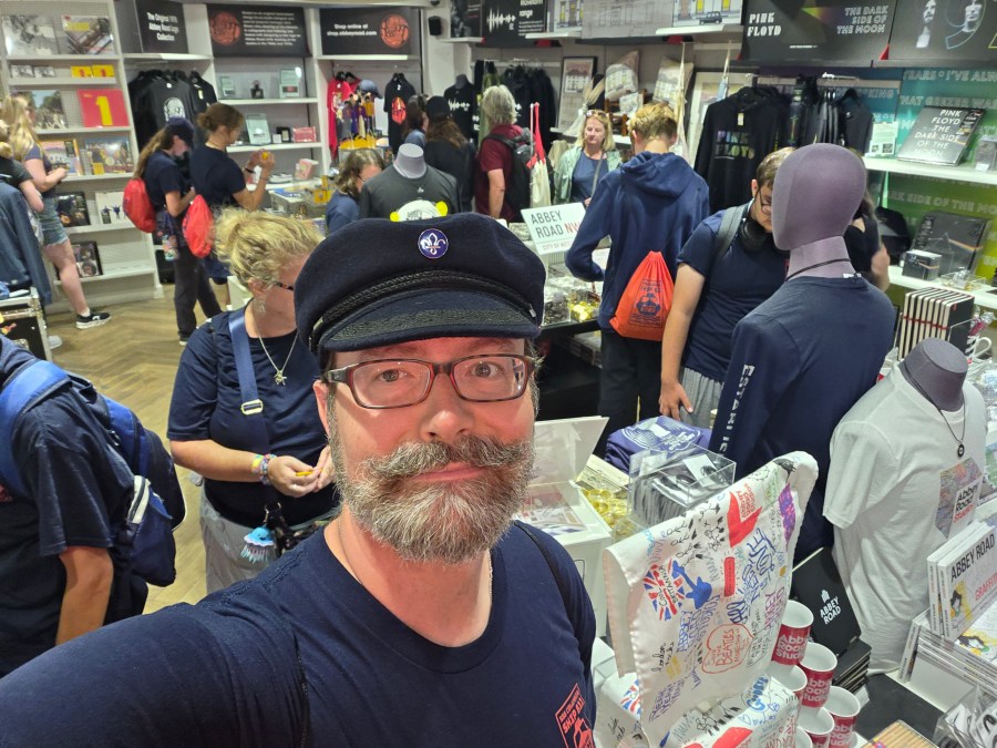 Jeffrey Fabiszewski wearing a navy mariner's cap with a Scouting fleur de lis pin inside the Abbey Road gift shop in London, surrounded by music merchandise.